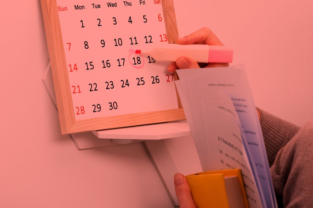  Abschnitt Bild: Eine Person kreist den 18. auf einem rosa Kalender mit einem rosa Marker ein und hält ein Buch.