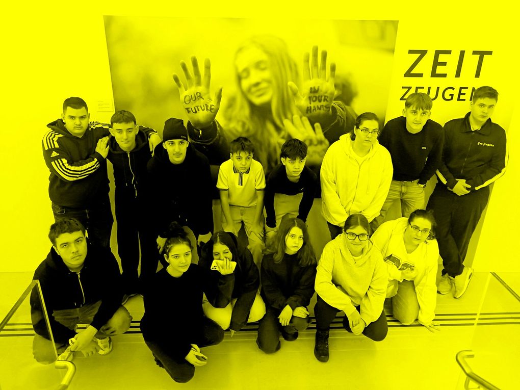 Abschnittsbild: Eine Gruppe junger Menschen posiert für ein Foto mit bemalten Händen in Gelb vor einem großen Poster mit dem Gesicht einer Frau und den Worten 'Unsere Zukunft'.