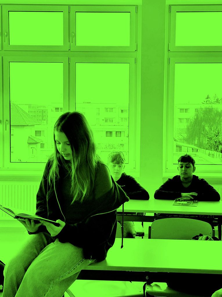 Abschnittsbild: Drei Schüler sitzen in einem Klassenzimmer mit grün getönten Fenstern, jeder beschäftigt sich mit einer eigenen Aktivität. Das Mädchen liest ein Buch, während die Jungen nachdenklich aussehen.