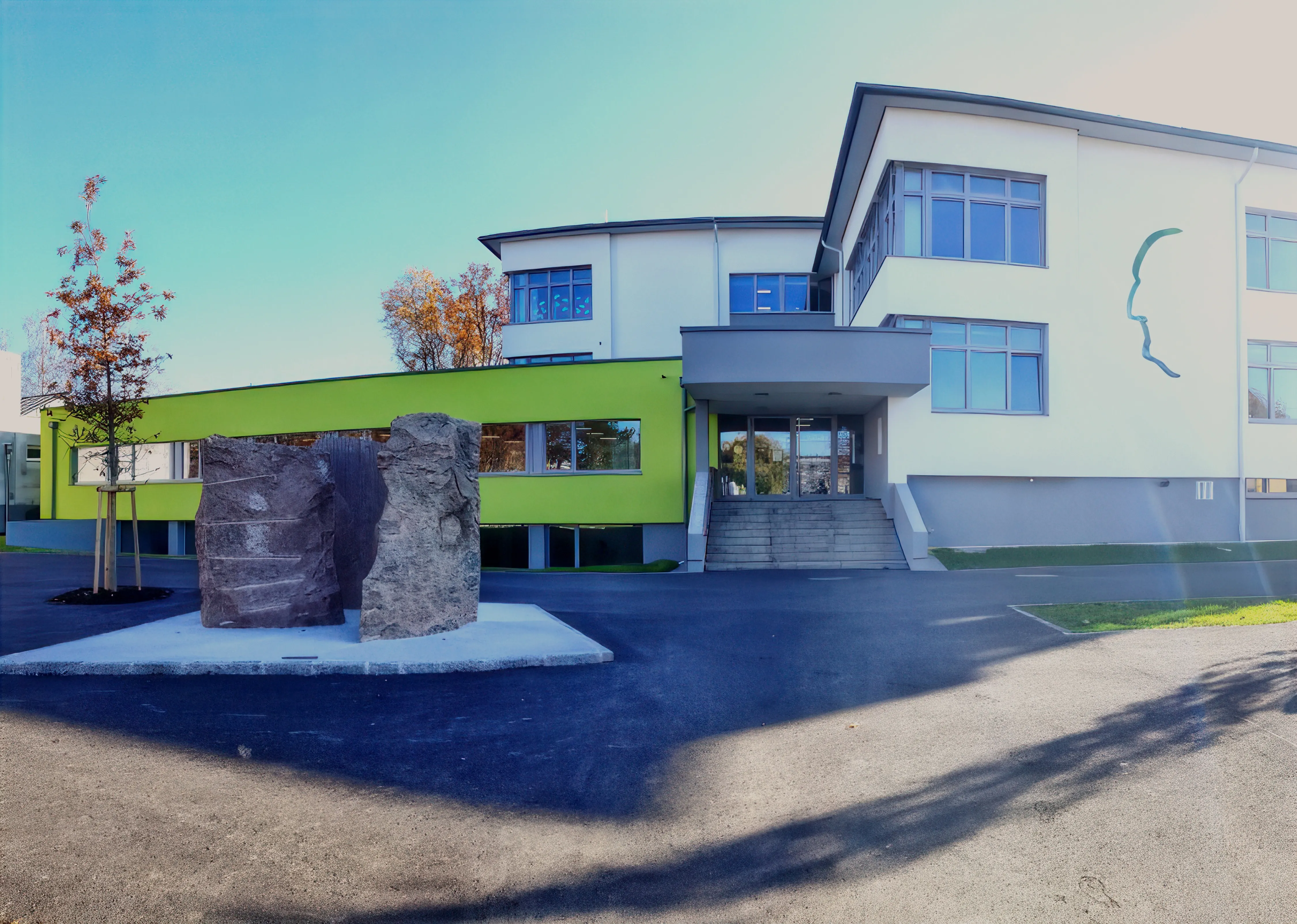 Ein modernes Gebäude mit grüner Fassade hat große Felsskulpturen davor, unter einem klaren blauen Himmel.
