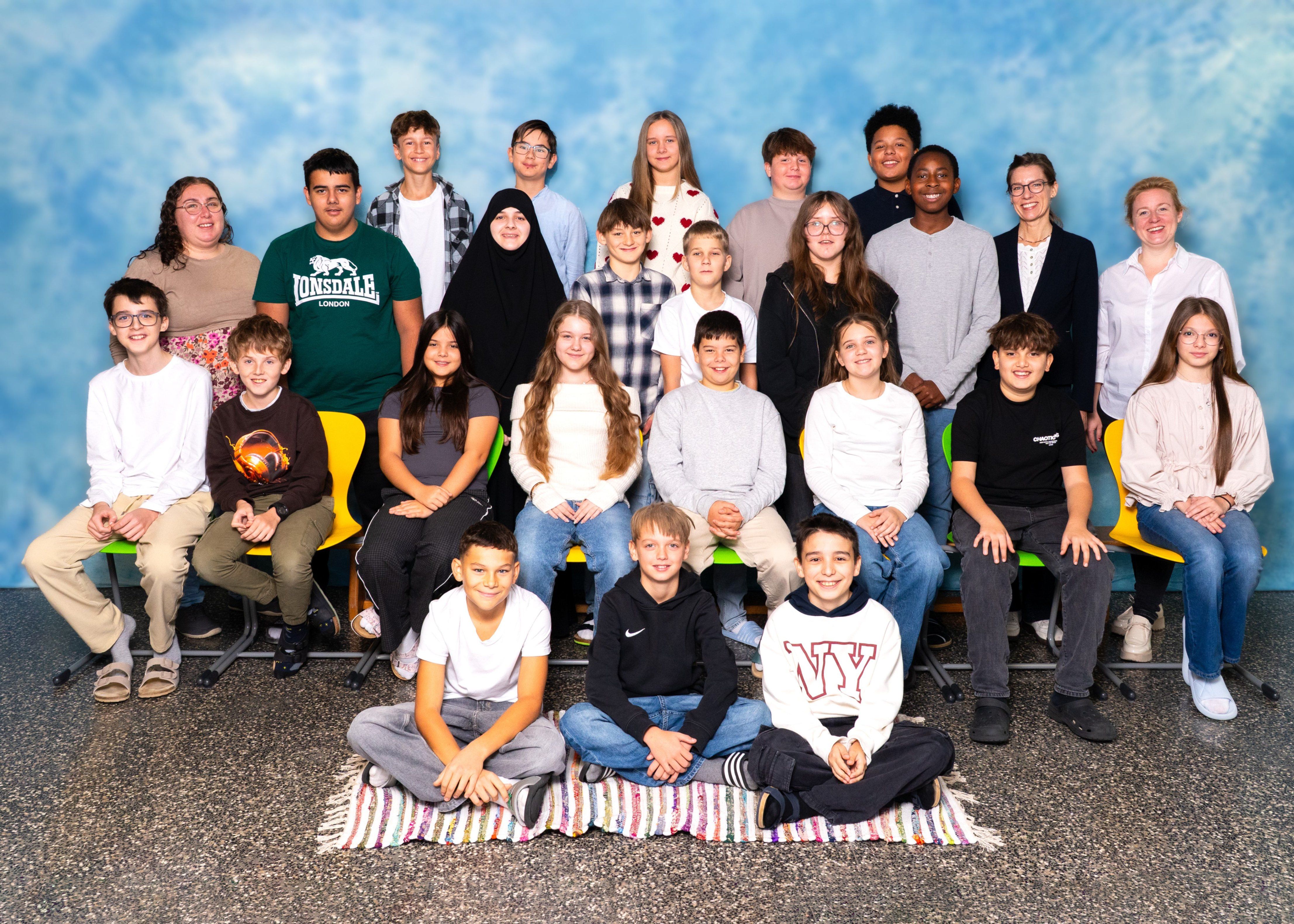 Eine Gruppe von Schülern und Lehrern posiert für ein Klassenfoto vor einem blauen Himmelshintergrund.