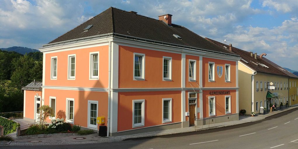  Abschnitt Bild: Ein großes orangefarbenes Gebäude mit schwarzem Dach steht am Straßenrand. Es hat weiße Fenster- und Türumrahmungen.