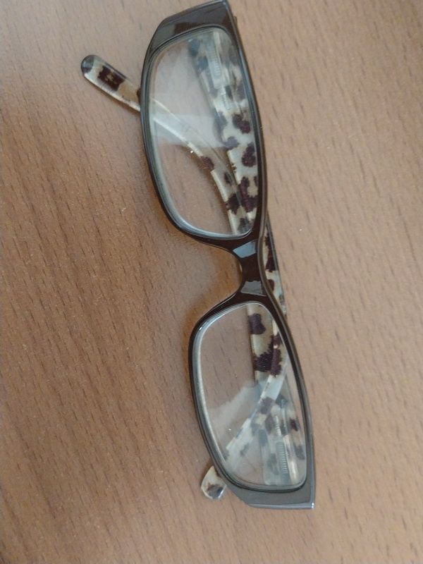 Ein Brillenpaar mit Leoparden-Print-Bügeln auf einer Holzoberfläche, die Gläser sind klar und der Rahmen besteht aus einem metallischen Material.