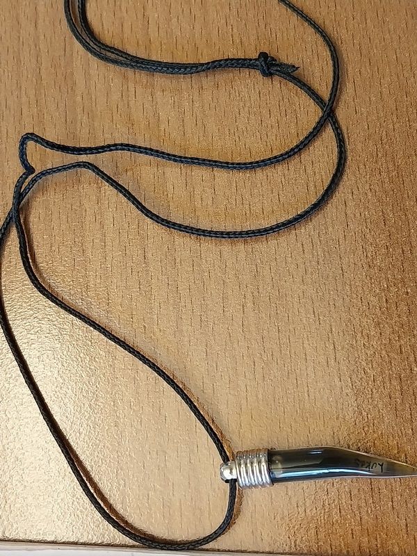 Eine Halskette mit einem schwarzen Kabel und einem silberfarbenen Metallanhänger liegt auf einer Holzoberfläche.