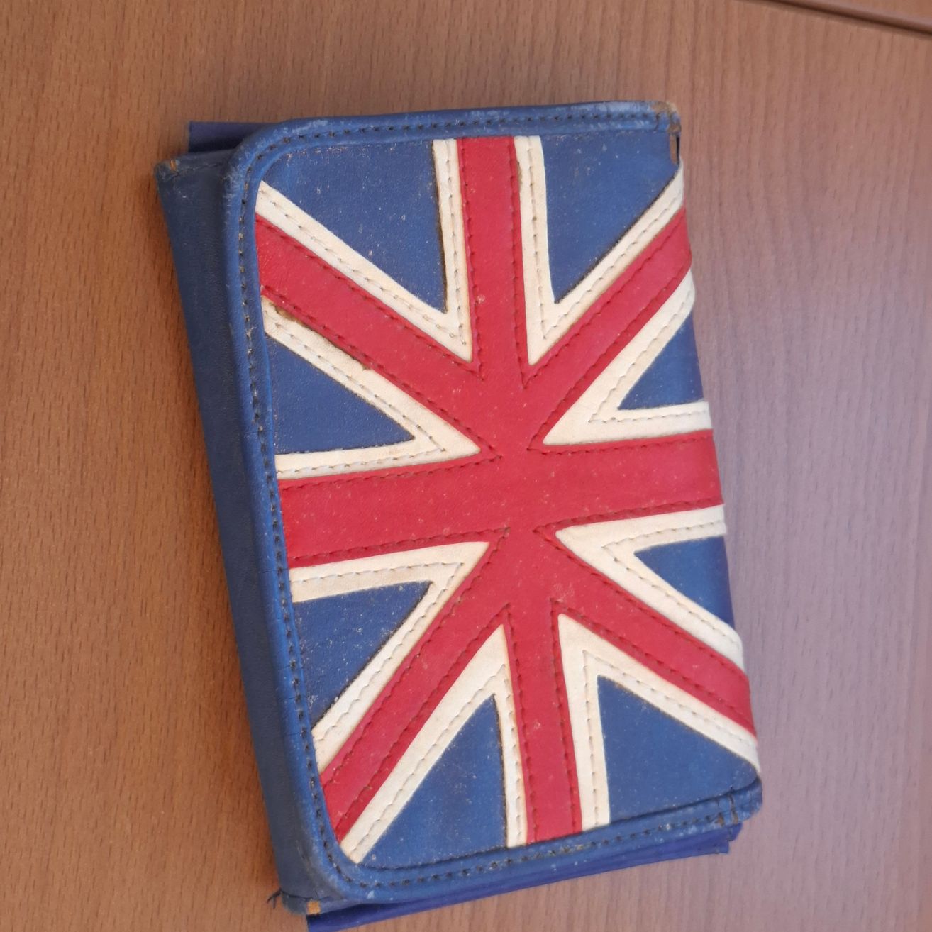 Ein blaues Portemonnaie mit Union Jack-Design. Das Portemonnaie liegt auf einer Holzoberfläche.