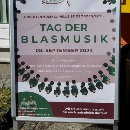 Ein Plakat für den Blasmusiktag am 8. September 2024 mit einer Gruppe von Musikern in traditioneller Kleidung. Die Veranstaltung beginnt um 10:00 Uhr mit einem Gottesdienst in der St. Georgen Kirche.