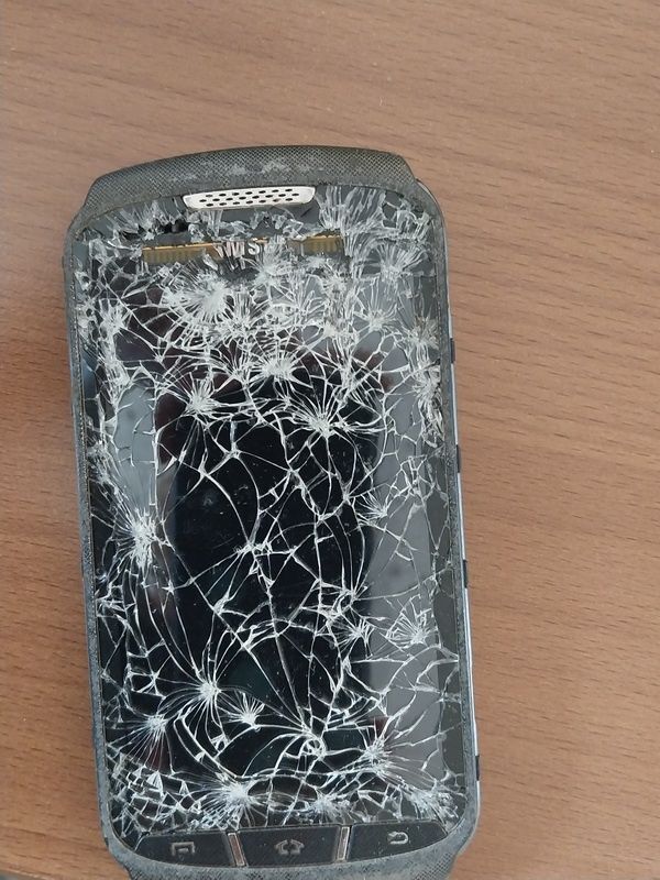 Ein Handy mit einem gesprungenen Bildschirm auf einem Holztisch.