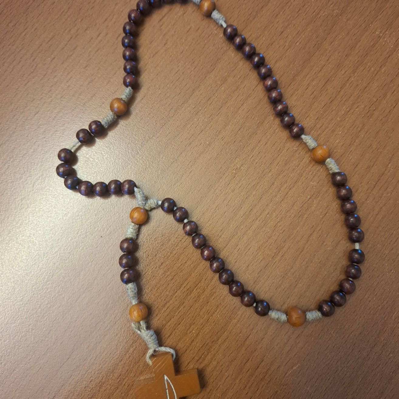 Eine hölzerne Rosenkranz mit braunen Perlen und einem Holzkreuz auf einer Holzoberfläche.