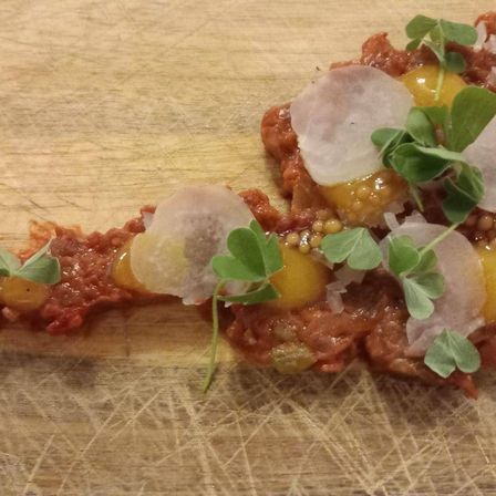 Ein Nahaufnahme eines Gerichts auf einer Holzoberfläche, bestehend aus einer roten Sauce mit Eiern, Perlen und grünen Kräutern.