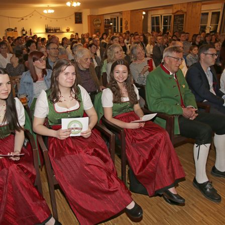 Eine Gruppe von Menschen sitzt in Stühlen in einem großen Raum. Sie schauen auf Papiere.