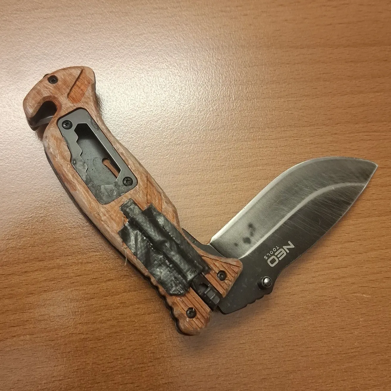Ein Nahaufnahme eines Taschenmessers mit holzfarbenem Griff und schwarzer Klinge, auf einer Holzoberfläche platziert.