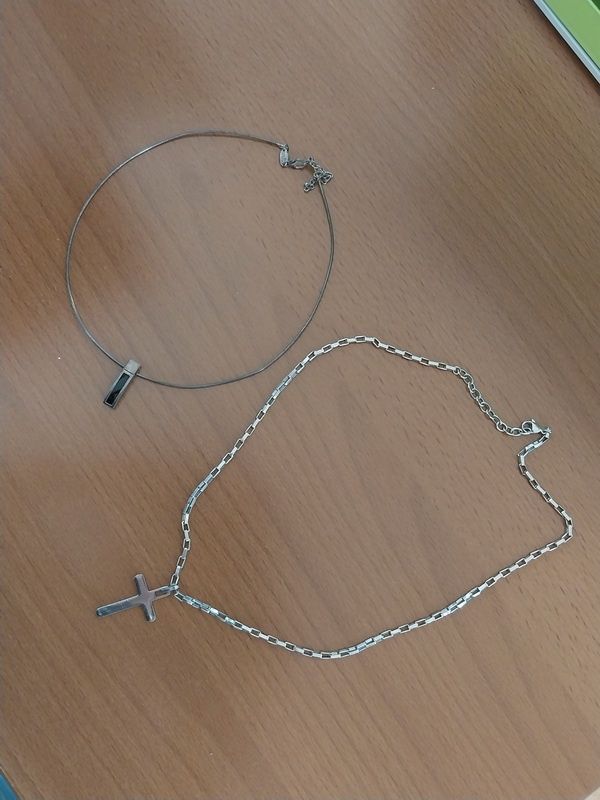 Zwei silberne Halsketten auf einem Holztisch, eine mit Kreuzanhänger und die andere eine Kette mit Anhänger.