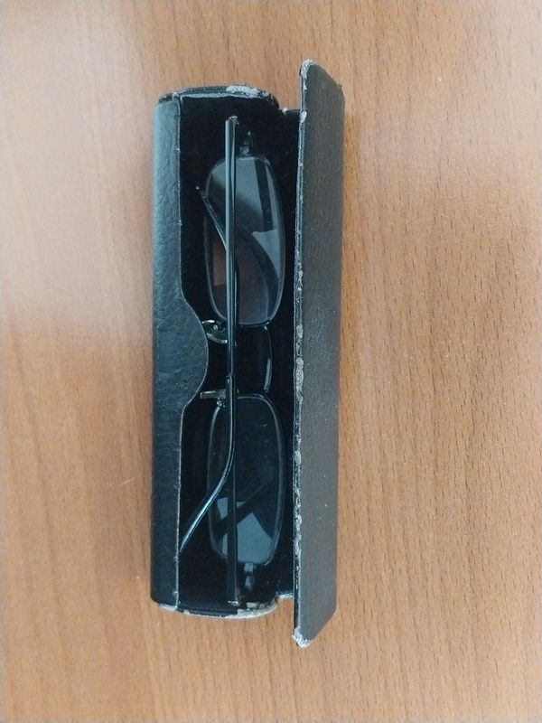 Eine schwarze Brillenbox mit einer Brille darin steht offen auf einer Holzoberfläche.