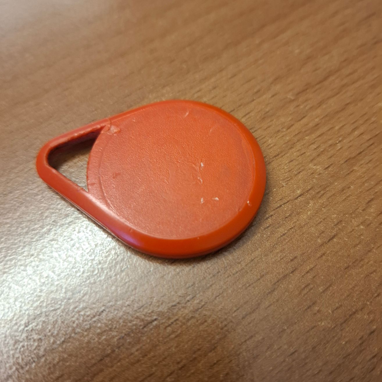 Ein Nahaufnahme eines orangefarbenen Kunststoff-Schlüsselanhängers mit Schlüsselloch, auf einer Holzoberfläche platziert.