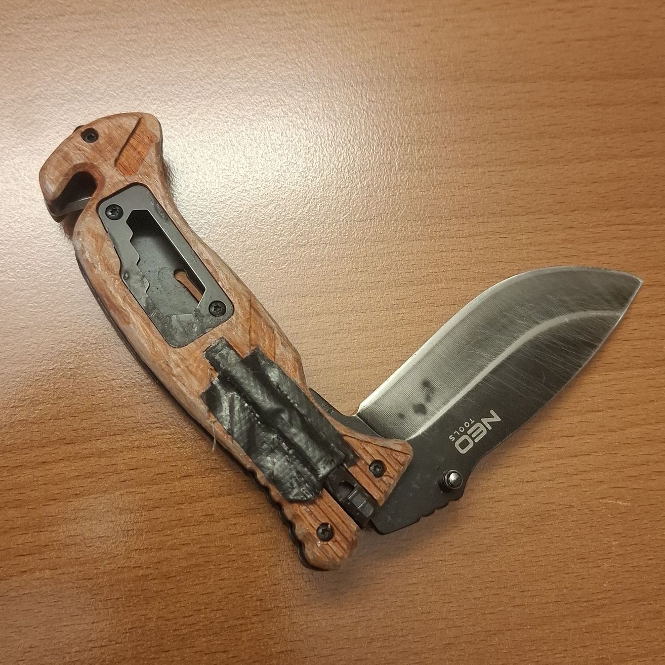 Ein Nahaufnahme eines Taschenmessers mit holzfarbenem Griff und schwarzer Klinge, auf einer Holzoberfläche platziert.