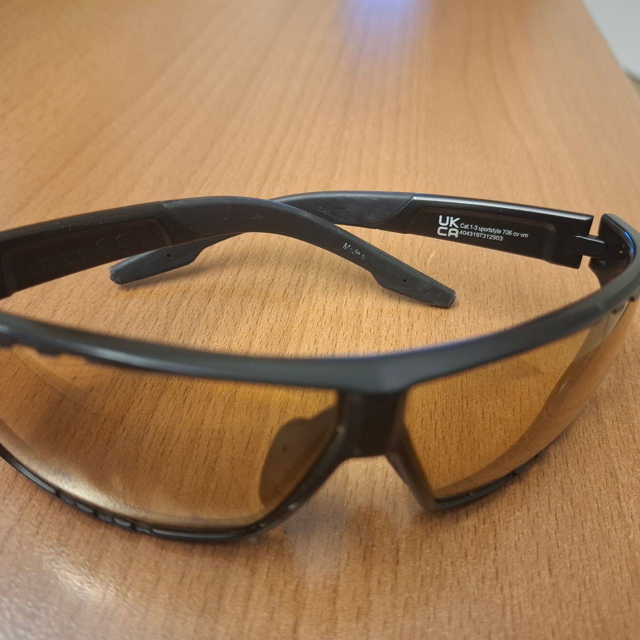 Ein Paar schwarze Schutzbrille mit braunen Gläsern auf einer Holzoberfläche.