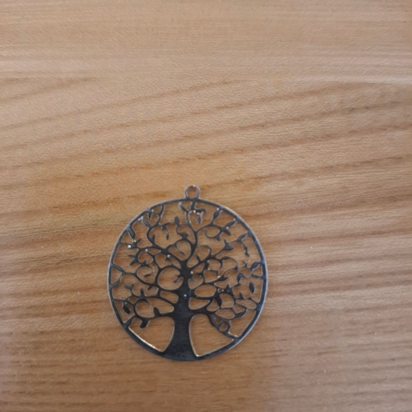 Ein silberner Anhänger mit Baumdesign auf einer Holzoberfläche.