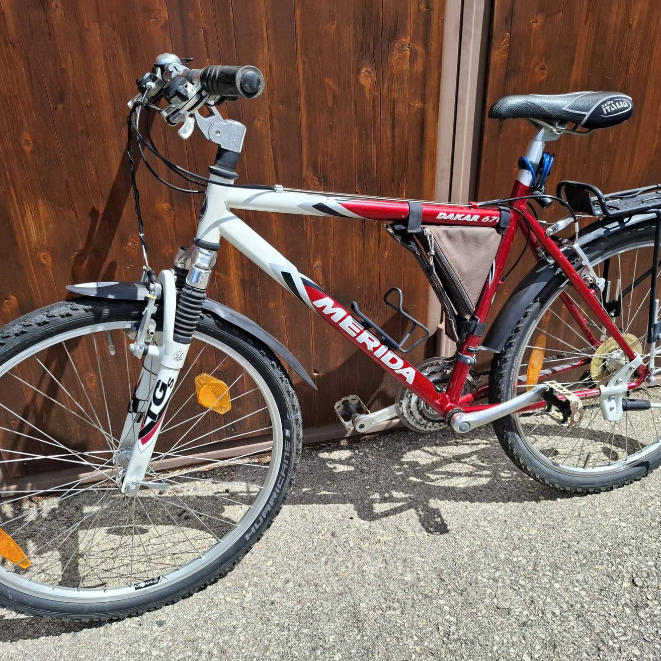 Ein rot-weißes Merida-Fahrrad mit der Aufschrift Dakar am Rahmen, geparkt an einer Holzwand.