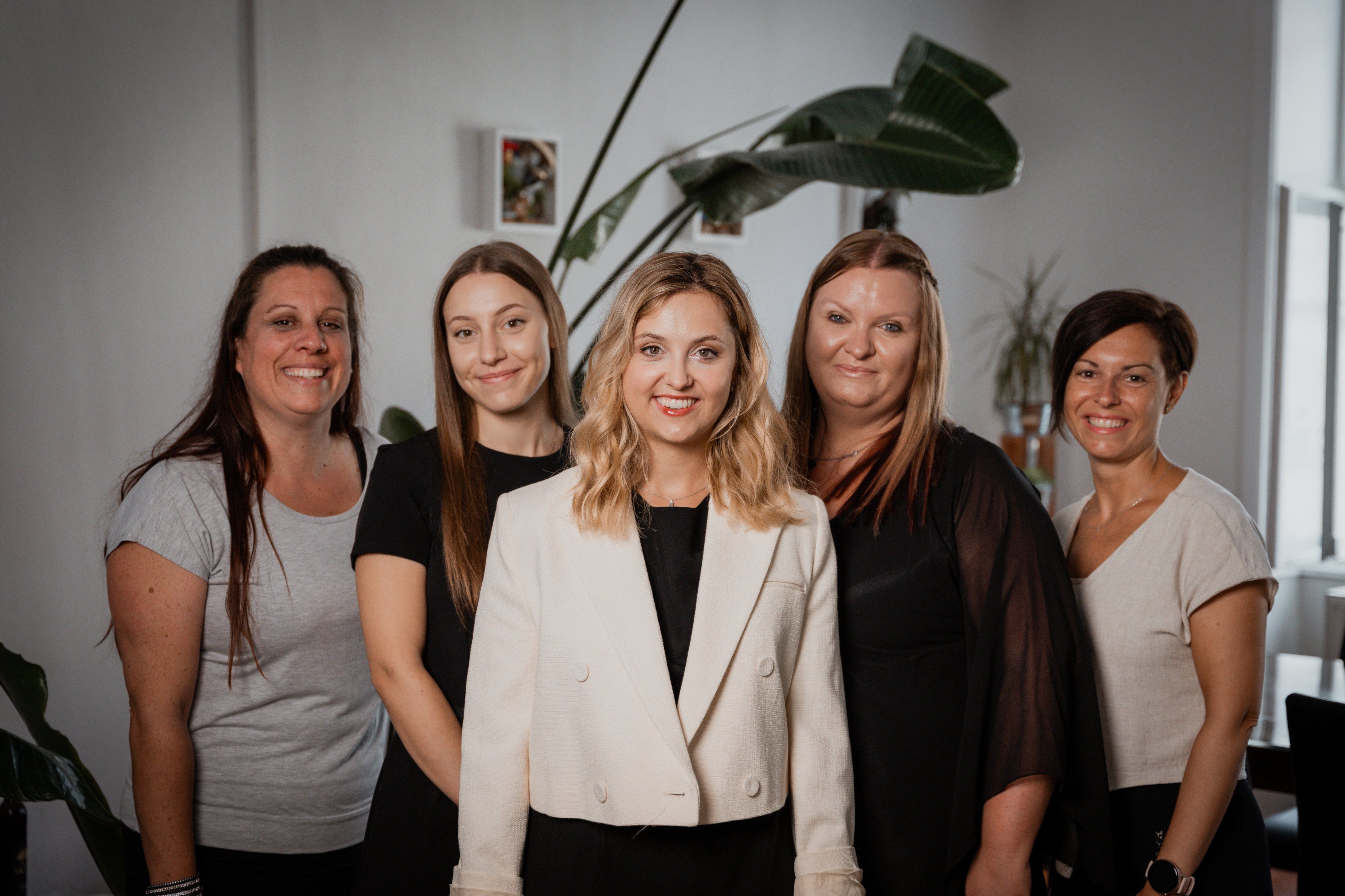Fünf Frauen posieren für ein Foto im Innenbereich mit einer großen Pflanze im Hintergrund. Sie alle lächeln und schauen in die Kamera.