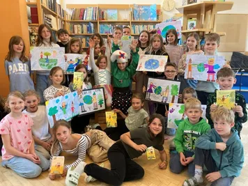 Kinder posieren in einer Bibliothek mit Zeichnungen der Erde und Zeichnungen auf ihren Händen für ein Foto. Einige der Zeichnungen haben die Worte 'Rette unseren Planeten' darauf.