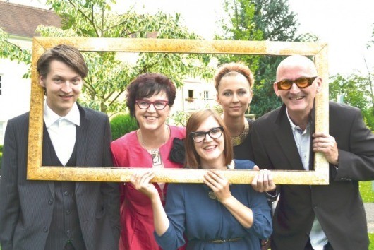 Eine Gruppe von Menschen steht in einem Fotorahmen im Garten. Sie lächeln für die Kamera, mit Bäumen und einem Haus im Hintergrund.