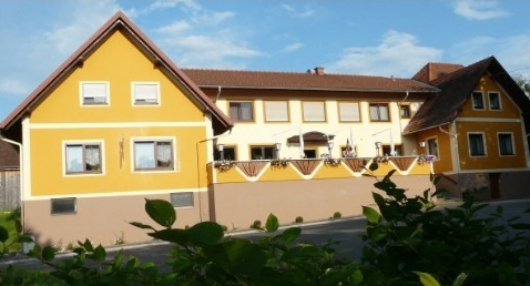 Ein großes gelbes Gebäude mit braunem Rand und mehreren Fenstern unter einem blauen Himmel mit Wolken.