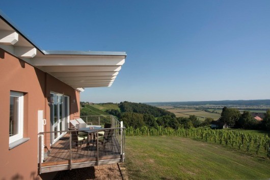 Ein Balkon mit Tisch und Stühlen mit Blick auf ein Weingut unter einem klaren blauen Himmel.