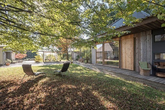 Ein Hinterhof mit zwei Liegestühlen, einer Holzterrasse und einem modernen Haus mit Glasfenstern und einer Holztür.