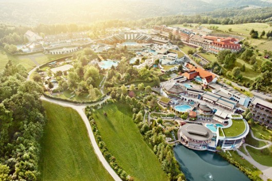 Ein Luftbild eines Resorts mit einem Fluss, einem Schwimmbad und verschiedenen Gebäuden, umgeben von grünen Bäumen und Gras.