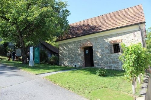 Ein altes Steingebäude mit einem braunen Dach und einer Tür in der Mitte, umgeben von grünem Gras und Bäumen.
