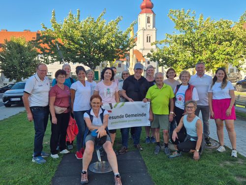 Eine Gruppe von Menschen in Freizeitkleidung posiert für ein Foto vor einer Kirche und hält ein Banner mit der Aufschrift 'esunde Gemeinde gemeinsam gestalten'.