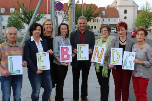 Eine Gruppe von Menschen hält Buchstaben hoch, die das Wort LEBEND vor einem Gebäude ergeben.