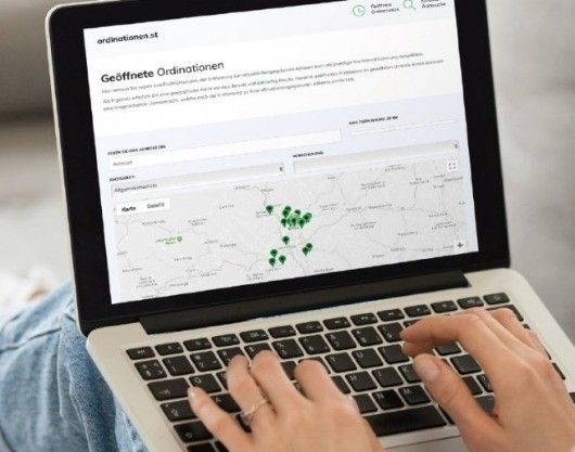 Eine Person benutzt einen Laptop mit einer offenen Karten-Website. Die Karte zeigt mehrere grüne Pins. Die Website heißt Geooffnete Ordinierungen.