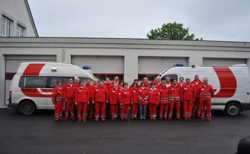 Eine Gruppe von Notfallsanitätern in roten Uniformen posiert für ein Foto vor ihren Fahrzeugen.