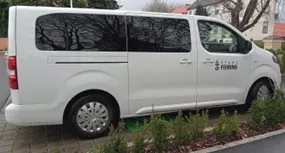 Ein weißer Lieferwagen mit getönten Fenstern ist auf einem Bürgersteig neben einem Bordstein geparkt. Der Lieferwagen hat ein Logo und Text an seiner Seitentür.