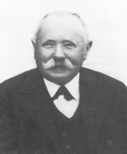 Schwarz-Weiß-Porträt eines älteren Mannes mit Schnurrbart, der einen formellen Anzug und eine Krawatte trägt.
