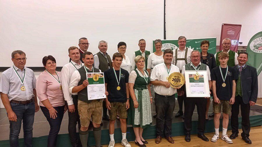 Eine Gruppe von Menschen posiert für ein Foto, einige tragen Medaillen und halten Urkunden und einen goldenen Pokal. Sie stehen auf einem Holzboden.