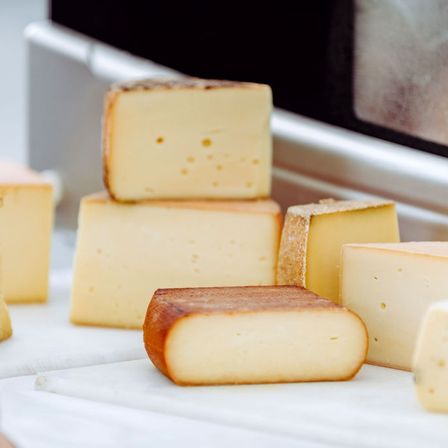 Mehrere Käseblöcke mit knuspriger Außenseite sind auf einer weißen Oberfläche angeordnet, wobei einige Blöcke übereinander gestapelt sind. Der Hintergrund ist leicht unscharf.