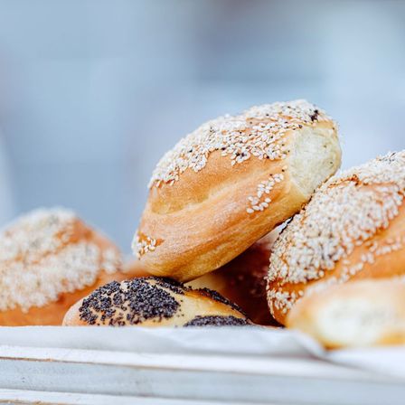 Ein Nahaufnahme von verschiedenen frisch gebackenen Brötchen, einige mit Sesam bestreut und andere mit Mohn, auf einer weißen Oberfläche präsentiert.