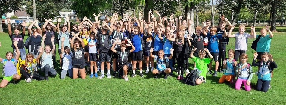 Eine Gruppe junger Athleten und Trainer posiert für ein Foto im Park, alle tragen Medaillen und lächeln.