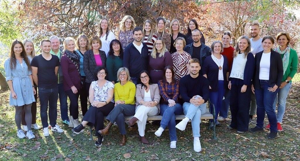 Eine Gruppe von Menschen, sowohl Männer als auch Frauen, posiert für ein Foto in einer Außenumgebung mit Bäumen im Hintergrund.