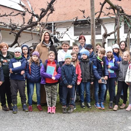 Eine Gruppe von Kindern und Erwachsenen posiert für ein Foto vor einem Gebäude mit Weinranken, in Winterkleidung und mit Büchern.