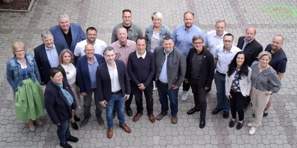 Eine Gruppe formell gekleideter Männer und Frauen steht in einem Kreis auf einem Ziegelpfad und lächelt für ein Foto.