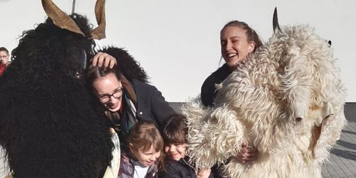 Eine Gruppe von Menschen in Kostümen, zwei mit Hörnermasken, lächeln und posieren für ein Foto mit zwei Kindern.