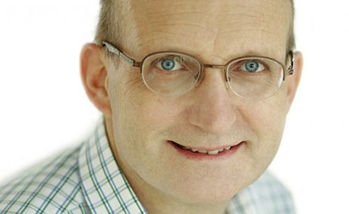Ein Nahaufnahme eines älteren Mannes mit Brille und kariertem Hemd. Er hat ein Lächeln im Gesicht.