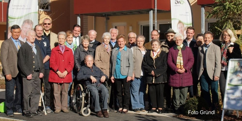 Eine Gruppe älterer Erwachsener, einige in Rollstühlen, stehen vor einem Gebäude. Sie lächeln und posieren für ein Foto.