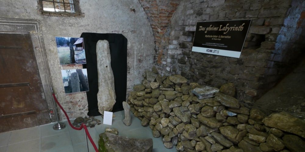 Ein Raum mit ausgestellten Steinen und Artefakten, mit einem schwarzen Schild 'Das geheime Labyrinth' und Fotos von Steinen.