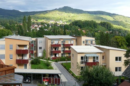 Ein Luftbild eines modernen Wohnkomplexes mit Balkonen, vor dem Hintergrund üppiger grüner Hügel und eines klaren Himmels.