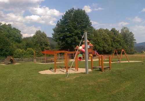 Ein Spielplatz mit Rutsche und Klettergerüst. Grüner Rasen und Bäume im Hintergrund.