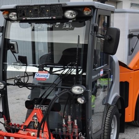 Orange-graues Stängl Citymaster 1800 Fahrzeug mit mehreren Lichtern, geparkt vor einem Gebäude.